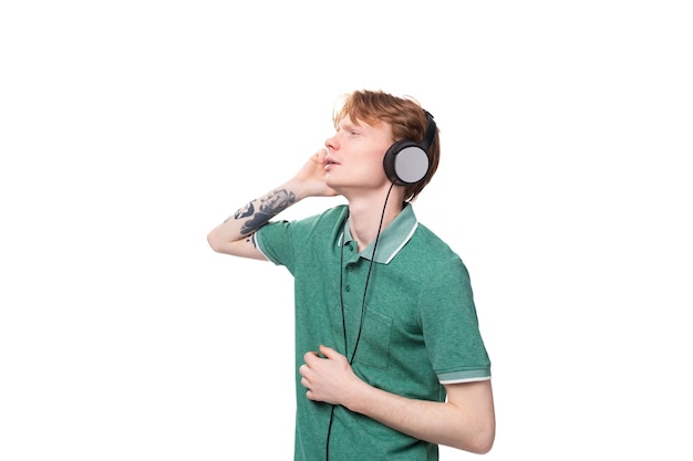 Een jonge man met rood haar gekleed in een groen t-shirt in draadloze grote koptelefoons danst en geniet