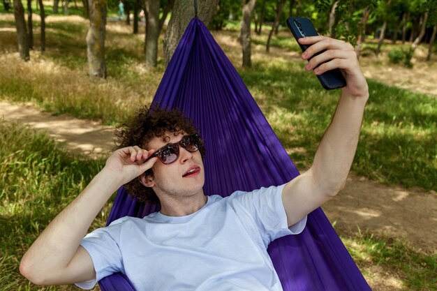 Foto een jonge man neemt een selfie op de telefoon en ontspant zich in een paarse hangmat in de natuur en geniet van de stilte