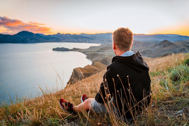 Een jonge man reist langs de bergkust bij zonsondergang Een man staat op een berghelling