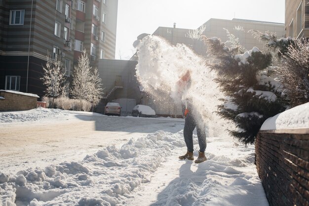 Een jonge man ruimt de sneeuw voor het huis op een zonnige en ijzige dag. De straat sneeuwvrij maken.