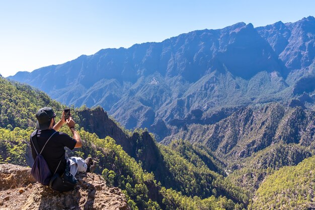 Een jonge man rust na een trekking op de top van La Cumbrecita zittend in het natuurlijke uitkijkpunt en het nemen van een foto met de mobiele telefoon, eiland La Palma, Canarische eilanden, Spanje