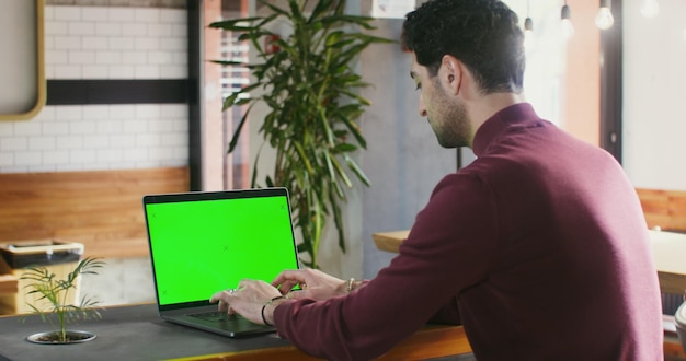 Een jonge man schrijft op een laptop met een groen scherm in een koffieshop