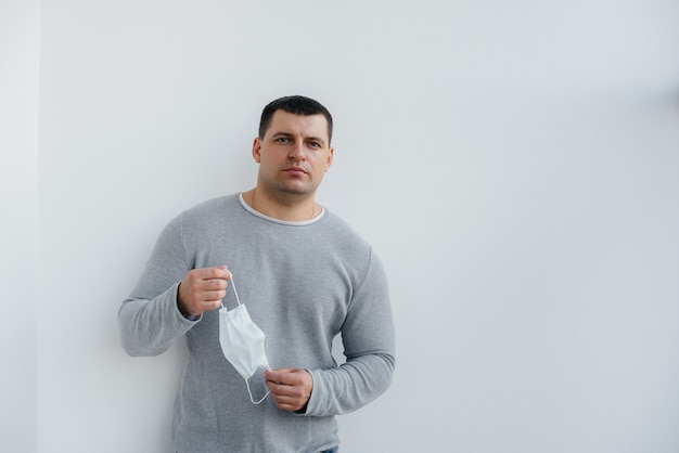 Een jonge man staat op een grijze achtergrond met een masker tijdens een quarantaine met vrije ruimte. Quarantaine in het masker