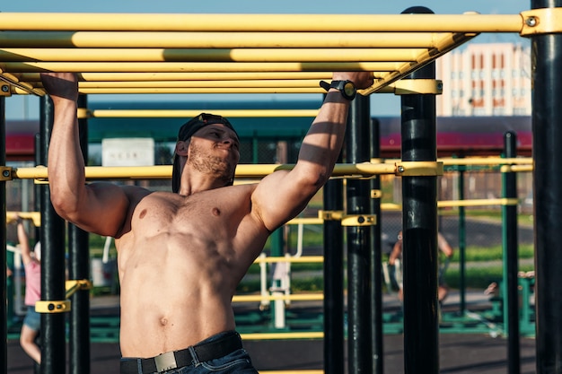 Een jonge man trekt zich omhoog op het sportveld, een atleet traint buiten in de stad