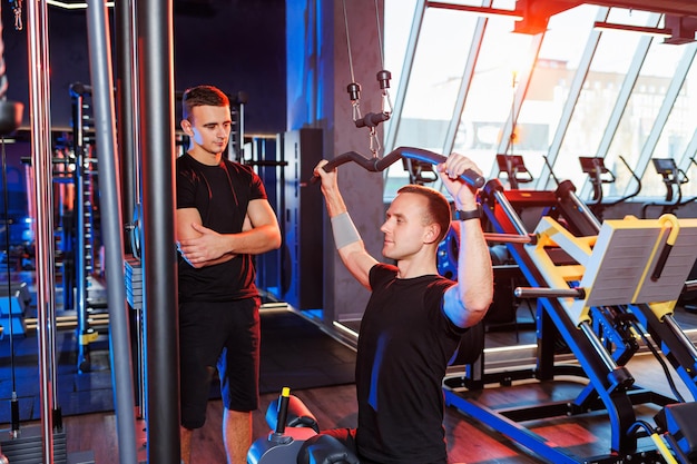 Een jonge man voert oefeningen uit in de sportschool onder toezicht van een trainer. Krachtige training door een knappe man. Gezonde levensstijl