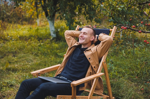 Foto een jonge man werkt buitenshuis op een laptop een jonge freelancer rust in het bos werken op afstand actieve recreatie in de zomer toerisme mensen concept man zittend op een stoel buiten