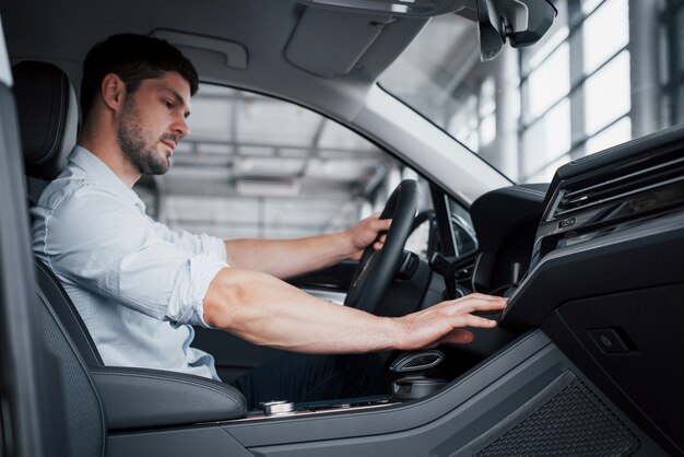 Een jonge man zit in een pas gekochte auto met zijn handen op een roer.