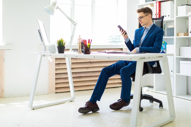 Een jonge man zit met een telefoon in zijn handen aan een tafel op kantoor.