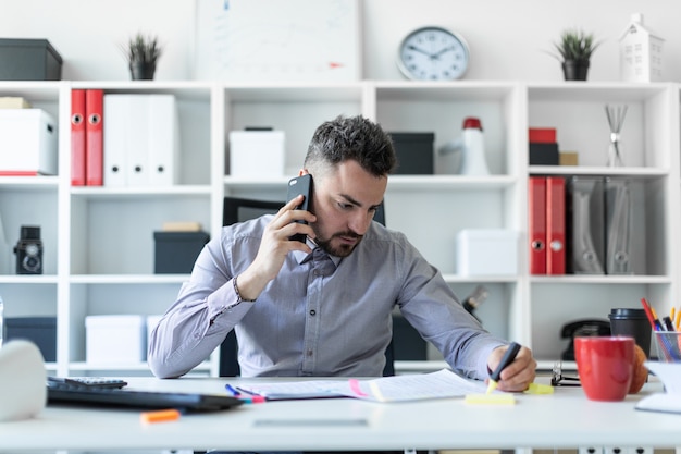 Een jonge man zit op kantoor, telefoneert en houdt een marker in zijn hand.