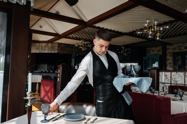 Een jonge mannelijke ober in een stijlvol uniform houdt zich bezig met het serveren van de tafel in een prachtig gastronomisch restaurant Een restaurant op hoog niveau Tafelservice in het restaurant