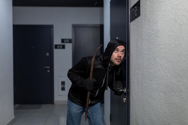 Foto een jonge mannelijke overvaller in donkere kleren staat voorzichtig en stil bij de deur van