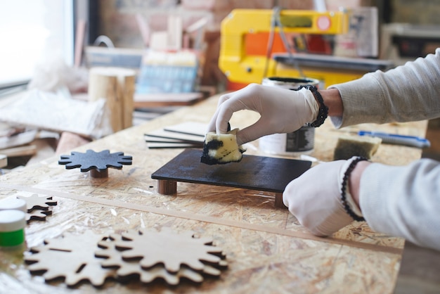 Een jonge meester schildert een houten stuk in een handgemaakte werkplaats