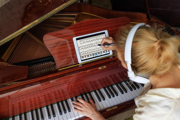 Een jonge meisjescomponist schrijft muziek op een tablet en speelt piano Modern concept