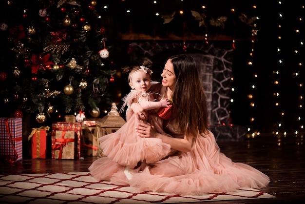 Een jonge moeder en dochter in bijpassende jurken versieren de kerstboom met nieuwe ballen