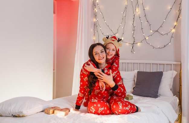 Een jonge moeder en dochter zitten op het bed in de slaapkamer in rode pyjama's in afwachting van de kerstvakantie en het nieuwe jaar. familie onderwijs.