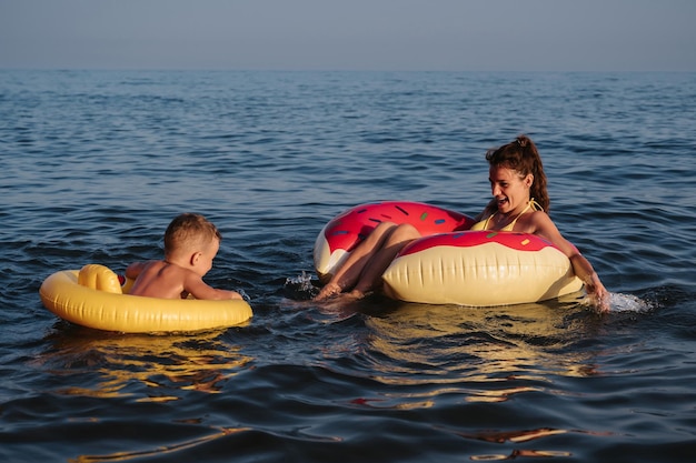 Een jonge moeder en een kind in zwemkringen hebben plezier en lachen tijdens het zwemmen in de zee