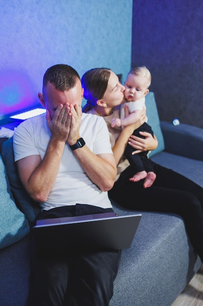 Een jonge moeder en vader zitten met hun pasgeboren zoon op de bank en kijken naar een film op een laptop Gezinsrelaties met een kleine baby Een gezinspaar met een kind thuis op de bank
