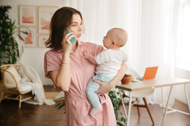 Een jonge moeder houdt een baby in haar armen en praat aan de telefoon