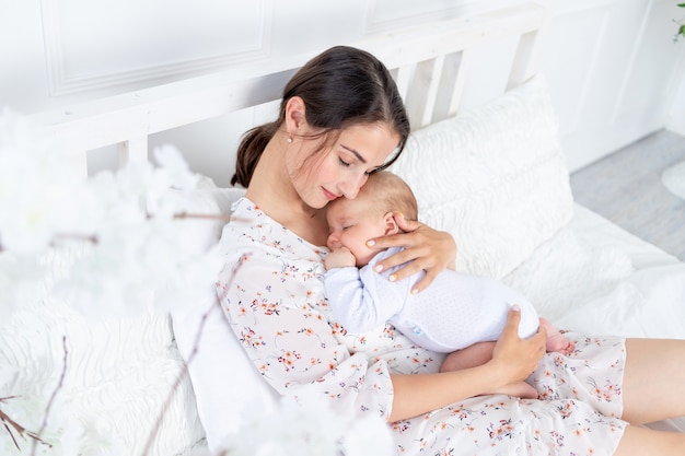 Een jonge moeder houdt een slapende pasgeboren baby in haar armen op het bed in de slaapkamer, het concept van moederschap en een gelukkig gezin.