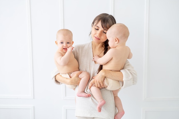 Een jonge moeder houdt twee tweelingbaby's in luiers vast in een lichte kamer thuis en lacht gelukkig moederschap met twee kinderen