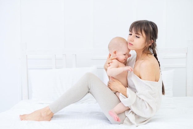 Een jonge moeder knuffelt en kust zachtjes een baby van zes maanden die hem in haar armen houdt liefde moeders zorg voor de baby gelukkig moederschap