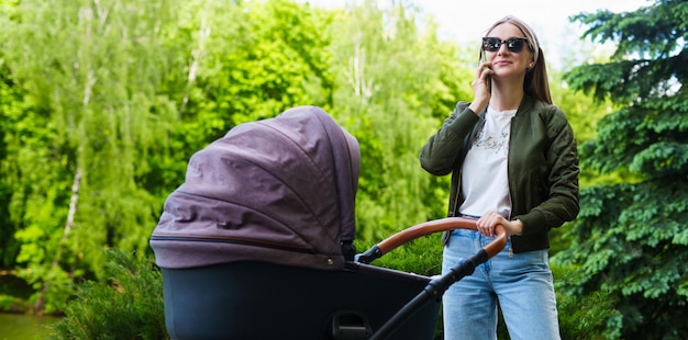 Een jonge moeder loopt met een kind dat in een kinderwagen slaapt en aan de telefoon praat