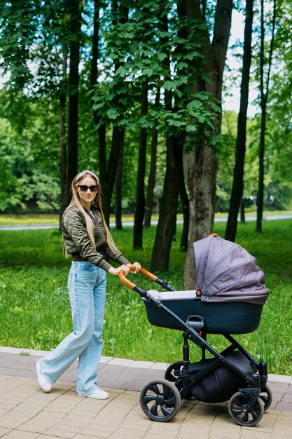 Een jonge moeder met een kinderwagen wandelt in de zomer met haar kind in het park