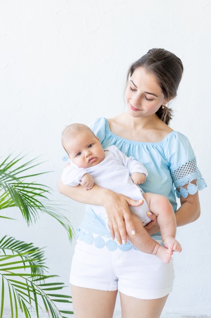 Een jonge moeder met een pasgeboren baby houdt het zachtjes in haar armen, knuffelt en bewondert het thuis, het concept van een gelukkig gezin