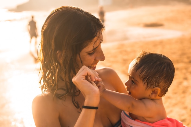 Een jonge moeder met haar baby genietend van een zonsondergang op een strand, Morro Jable, gemeente Pajara ten zuiden van Fuerteventura, Canarische Eilanden. Spanje