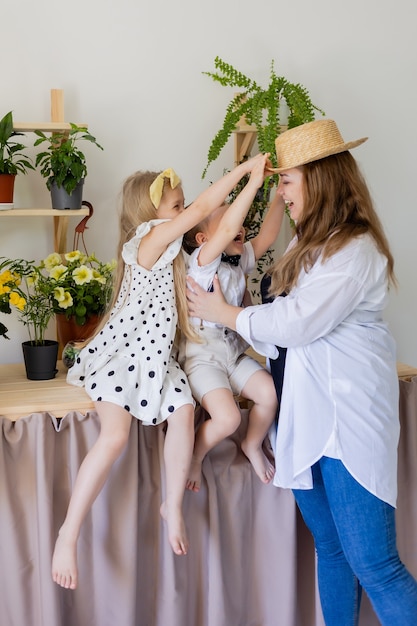 Een jonge moeder met haar zoon en dochter lacht knuffels en speelt binnen met huisbloemen