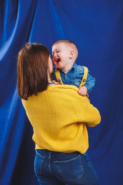 Een jonge moeder speelt met haar kind op een blauwe achtergrond Familierelatie met het kind Een kind opvoeden dat met een kind speelt