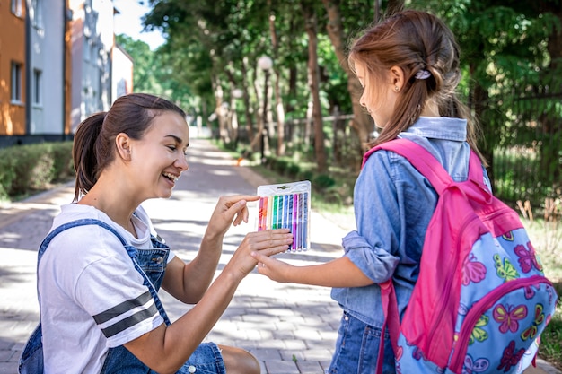 Een jonge moeder ziet haar dochtertje naar school gaan en geeft ze gekleurde stiften.