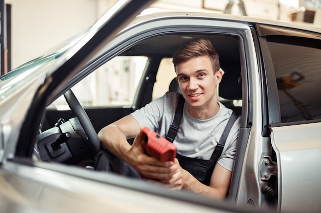 Een jonge monteur zit in een auto terwijl hij deze controleert.