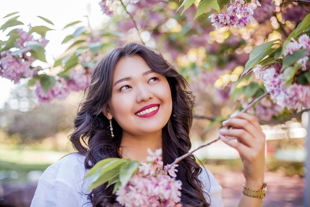 Een jonge mooie Aziatische vrouw in een witte jurk loopt in een bloemrijk park