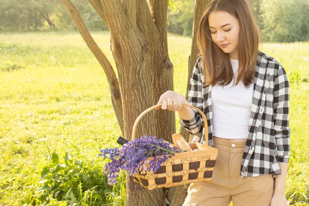 Een jonge, mooie blonde blanke vrouw houdt een picknickmand vast met bloemen, voedselwijn