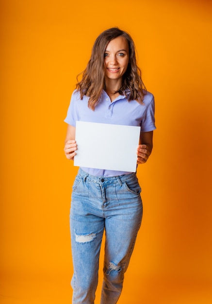 Een jonge mooie blonde in een blauw T-shirt en spijkerbroek houdt een wit vel papier in haar handen. ruimte kopiëren.