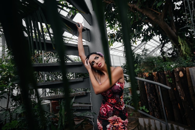 Een jonge mooie brunette poseert in de buurt van een wenteltrap in de botanische tuin tussen het dichte struikgewas van het tropische bos.