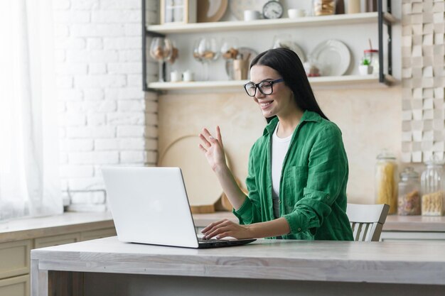 Een jonge, mooie brunette vrouw met een bril en een groen shirt praat tijdens een videogesprek met