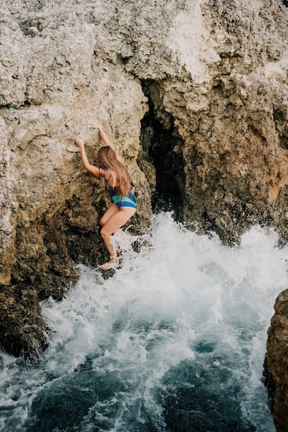 Een jonge mooie gebruinde vrouw met lang haar in blauwe bikini zittend op rotsen in de buurt van blauwgroen clear
