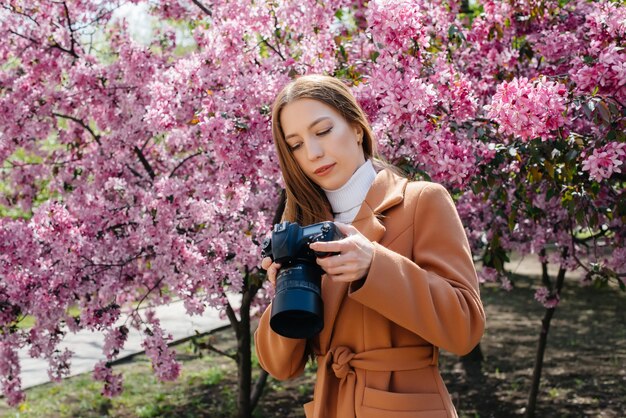 Een jonge mooie meisjesfotograaf loopt en maakt foto's tegen een bloeiende appelboom. Hobby's, recreatie.