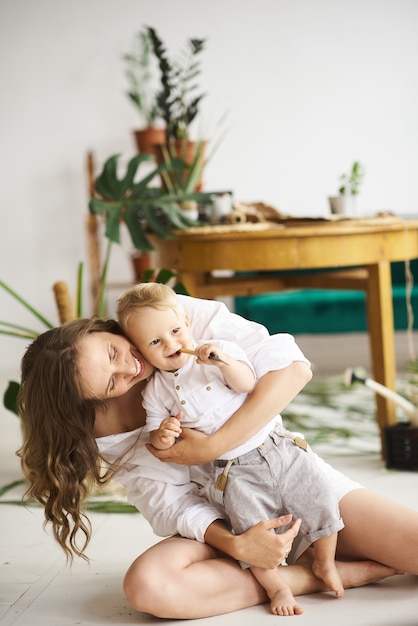 Een jonge mooie moeder die met haar baby op de vloer op een achtergrond van installaties en groene bank speelt