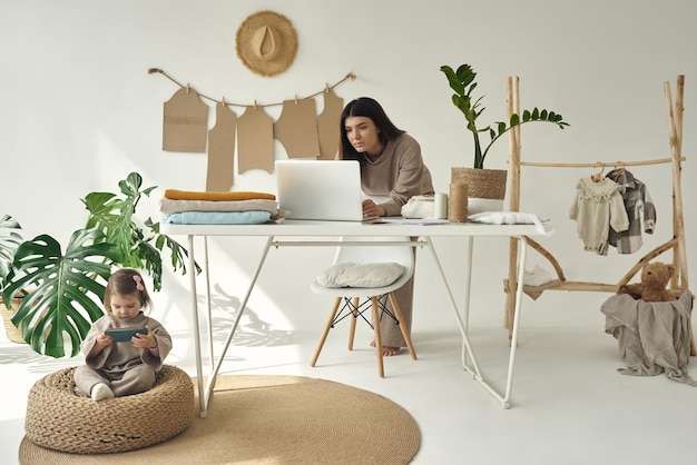 Een jonge, mooie naaister die thuis kleding maakt Vrouw staat aan tafel en werkt op een laptop