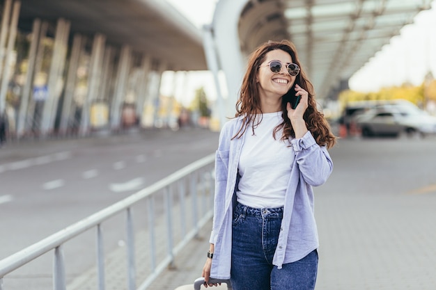 Een jonge mooie studente verlaat de luchthaven in een nieuwe stad en wacht op een taxi