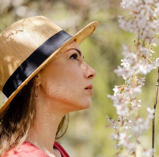 Een jonge mooie vrouw close-up in een strooien hoed bewondert de witte heldere kersenbloesems in de lentetuin