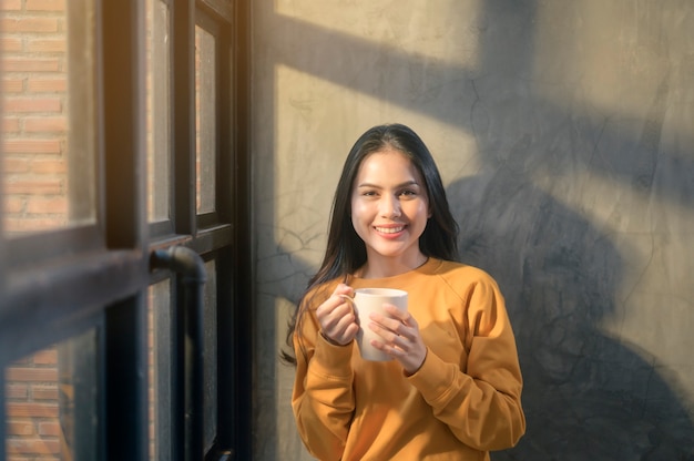 Een jonge mooie vrouw die in zonneschijnlicht thuis van haar ochtendkoffie geniet