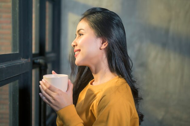 Een jonge mooie vrouw die in zonneschijnlicht thuis van haar ochtendkoffie geniet