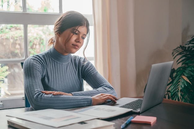 Een jonge mooie vrouw die thuis op tafel studeert en huiswerk doet Vrouwelijke tiener die laptop of computer gebruikt die binnenshuis op het net surft