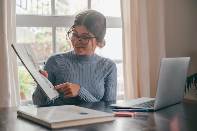 Een jonge mooie vrouw die thuis op tafel studeert en huiswerk doet Vrouwelijke tiener die laptop of computer gebruikt die binnenshuis op het net surft