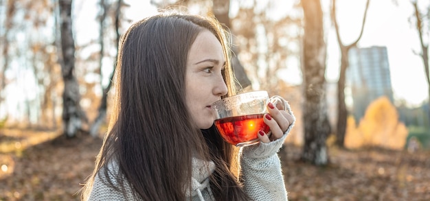 Een jonge mooie vrouw drinkt hete thee in een herfst geel park in het licht van de zonsondergang