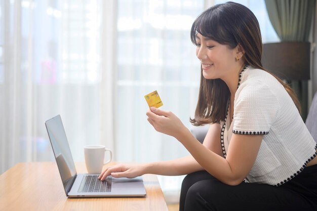 Een jonge, mooie vrouw gebruikt thuis een creditcard voor online winkelen op een internetwebsite